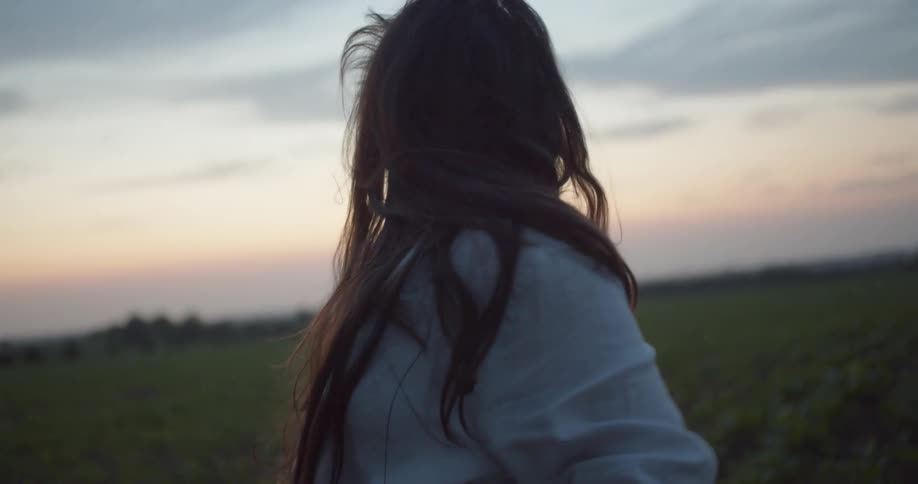 Woman dances in crop field with red sky sitting on horizon over forest