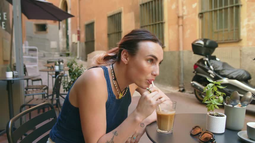 A woman sits at an outdoor cafe and drinks an iced coffee