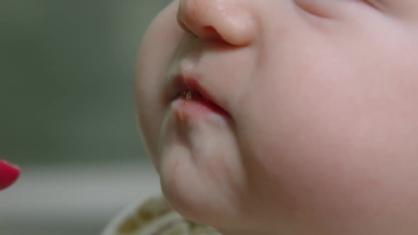 A baby being fed with a red spoon