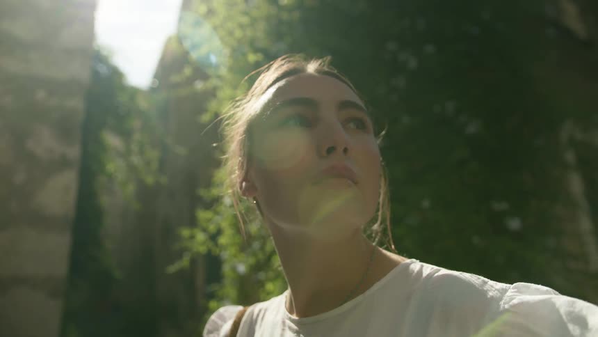 A woman is standing outside looking around as the sun shines on her face