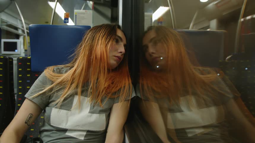 A woman sitting on a bus next to a window with her reflection