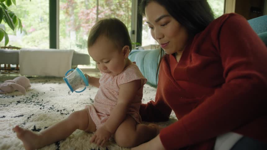 A woman is lying on a carpeted floor playing with her baby and laughing