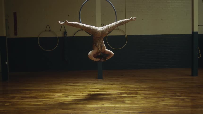Female aerialist spins on hoop floating on air performing routine in wood floored studio