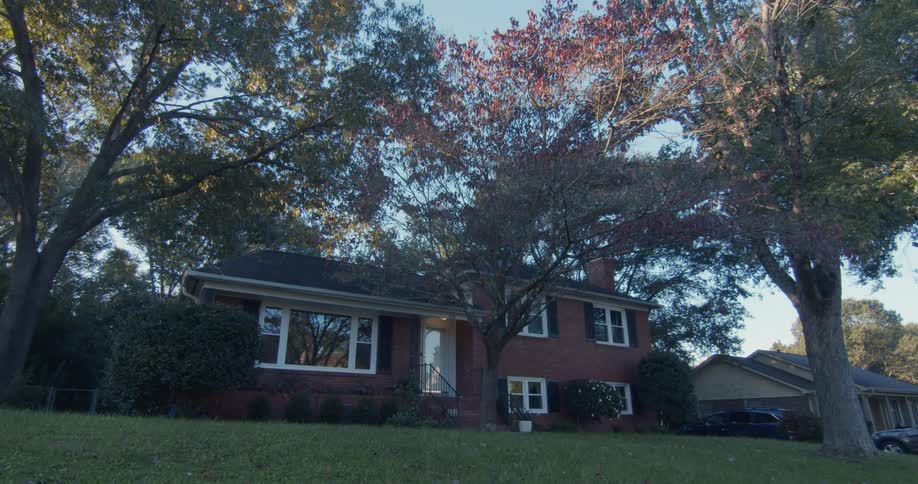 A large brick house sits on a well landscaped lot in a neighborhood as the sun goes down