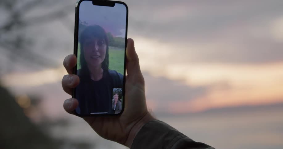 A man and woman are blowing kisses outside over a cell phone video call