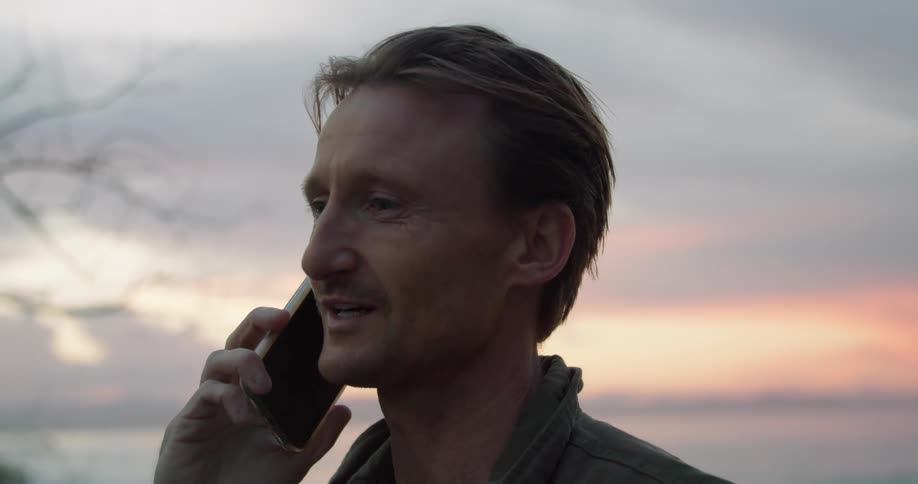A man laughs while talking on the phone while standing near the ocean
