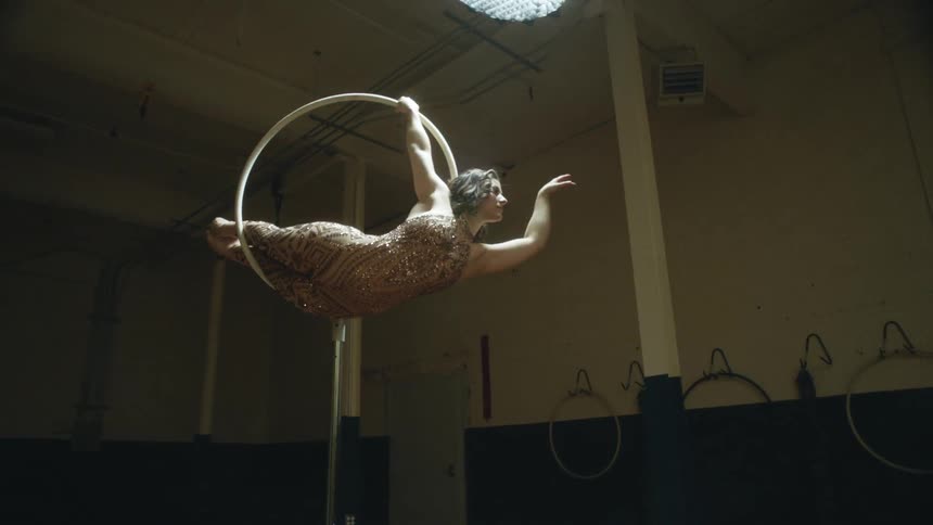 A woman hangs from a ring in the gym