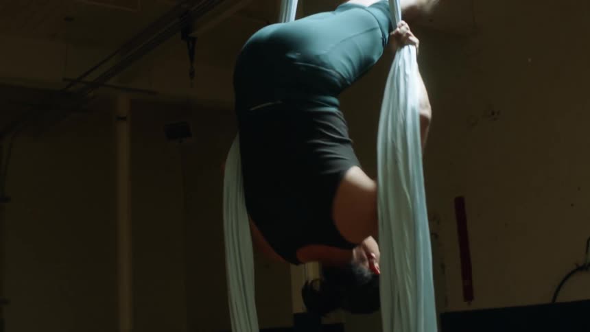 A male acrobat is hanging and spinning on two aerial silk ropes