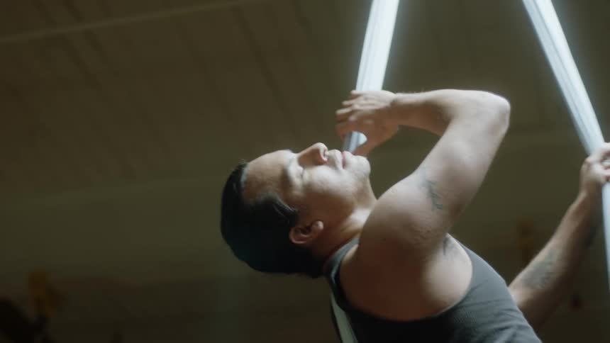Male aerialist holds onto fabric hanging from ceiling as he rotates and performs