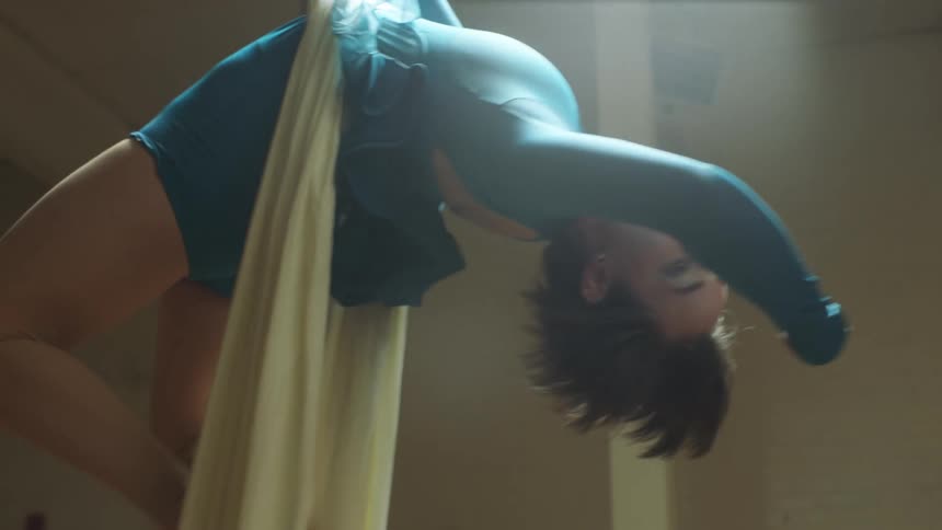 A female acrobat is hanging and bending from two aerial silk ropes