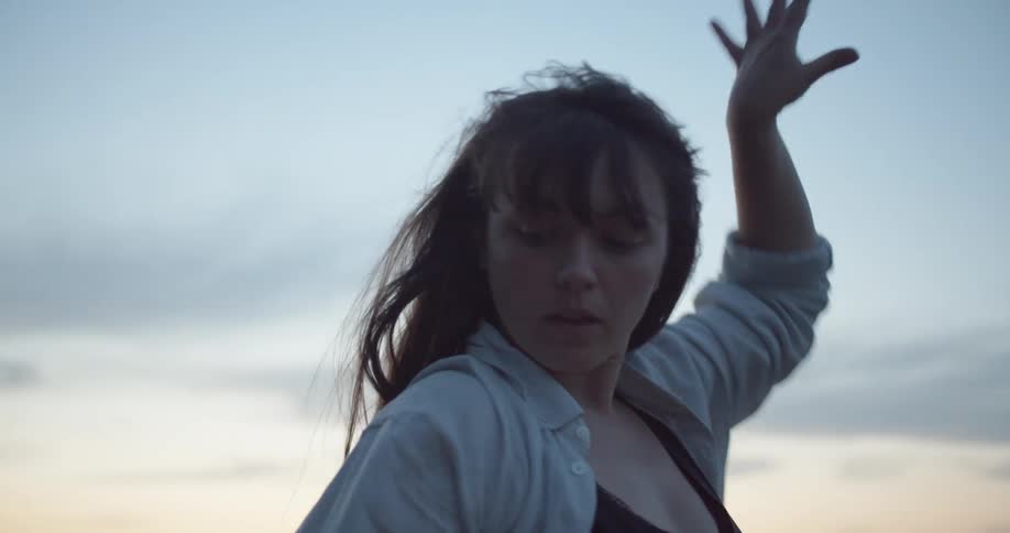 A woman moves her arms in a wave as she belly dances outside