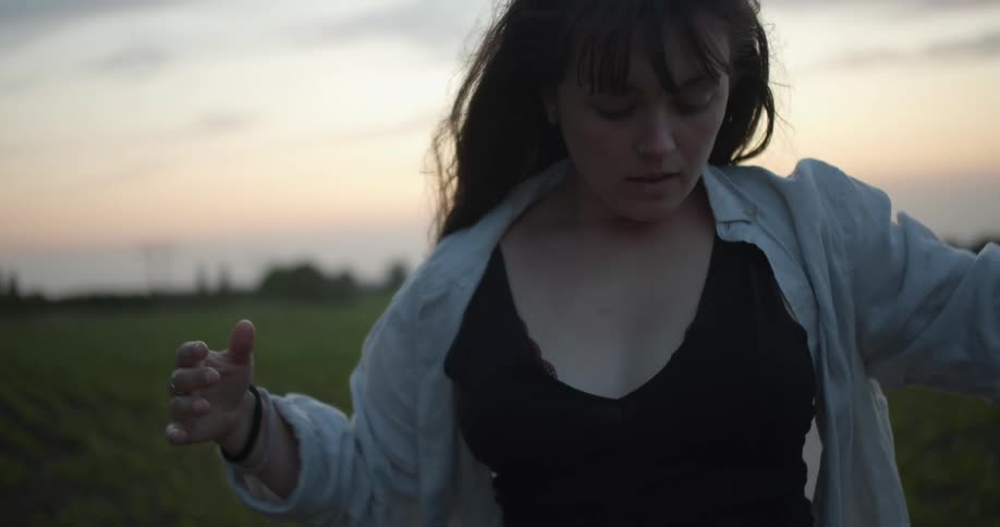 A woman dancing with a grassy field sky and clouds in the background
