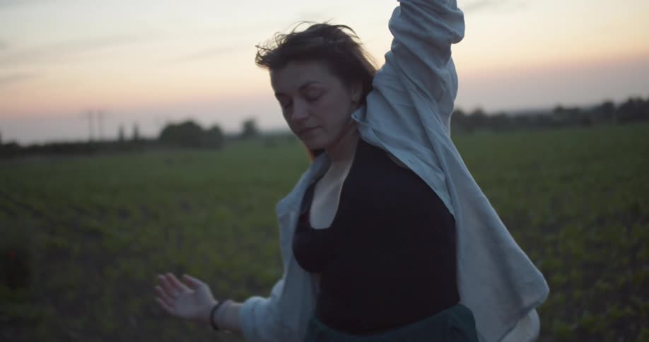 A young woman with long brown hair dancing in a rural field at sunset
