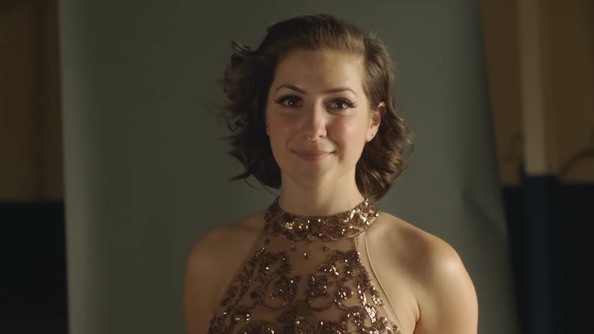 A woman is standing smiling and wearing a fancy gold sequin outfit and a gold ring in her nose