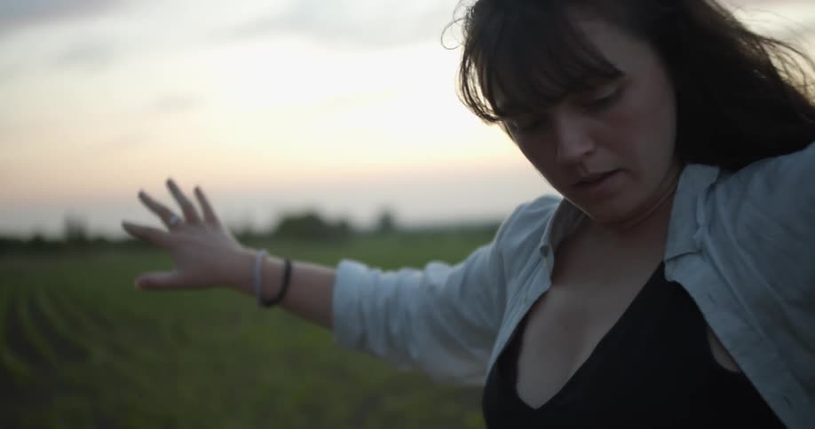Woman moves through dance routine with crops in background and red sky sitting over horizon