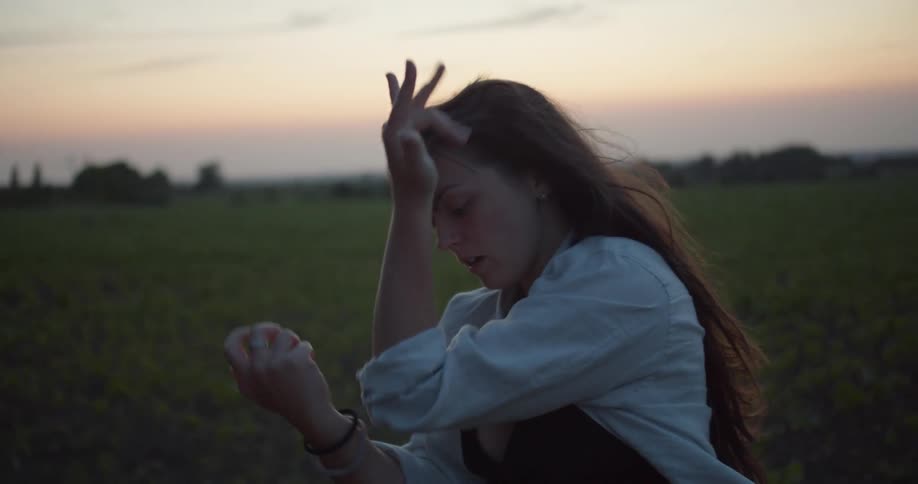 A woman dancing with a grassy field trees the sky and clouds in the background