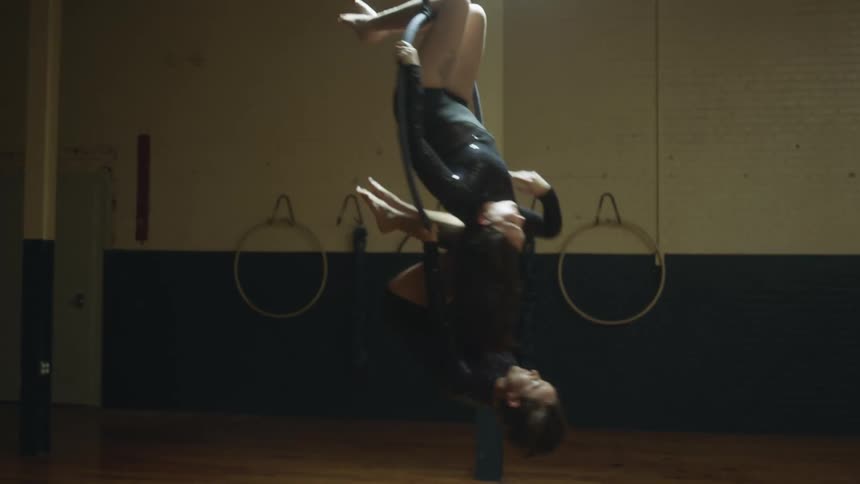 Pair of female aerialists practice routine on hoops in studio