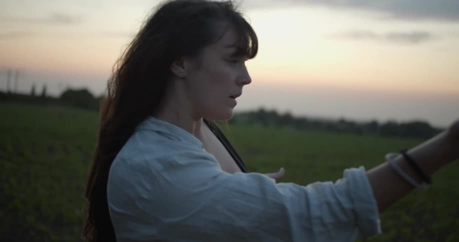 A woman is performing a modern dance outdoors next to crops on farmland at dusk