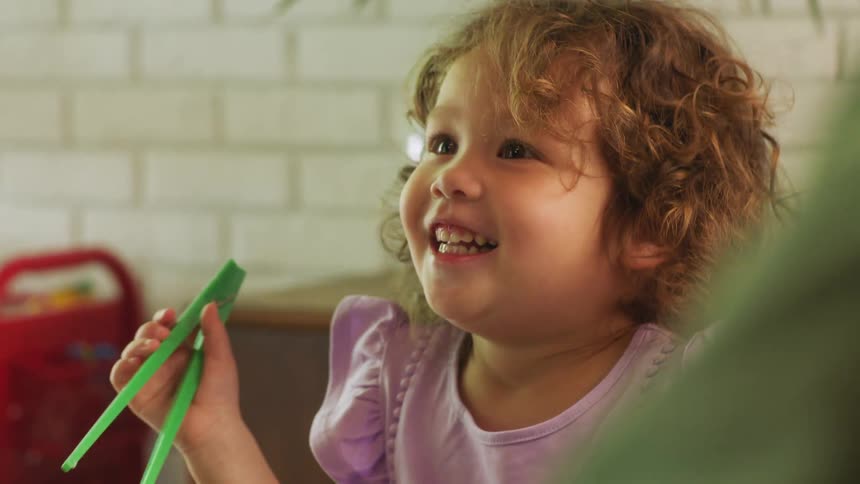 A child is holding green chopsticks and laughing