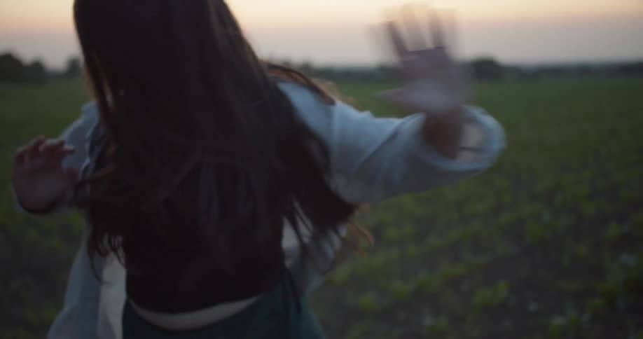 Woman dances and jumps near crops in field with red sky in background