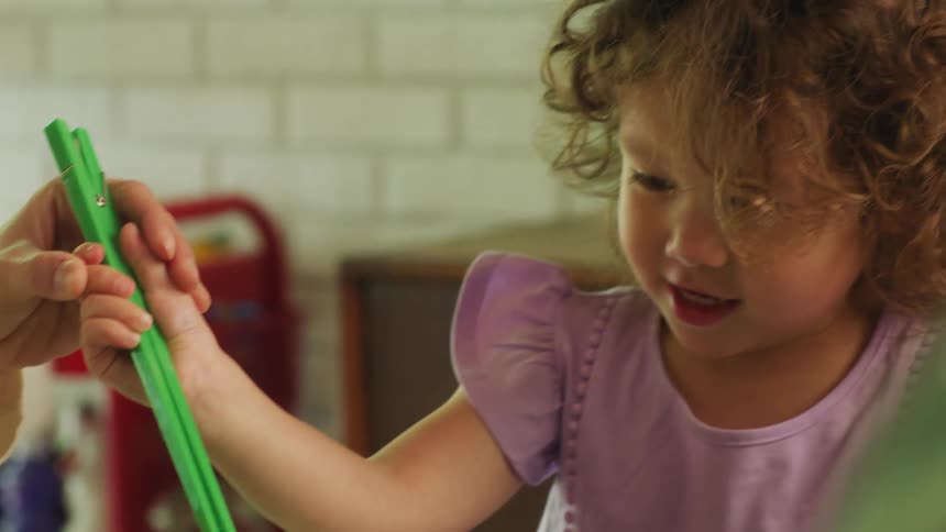 A little girl is learning to use chopsticks with the help of an adult