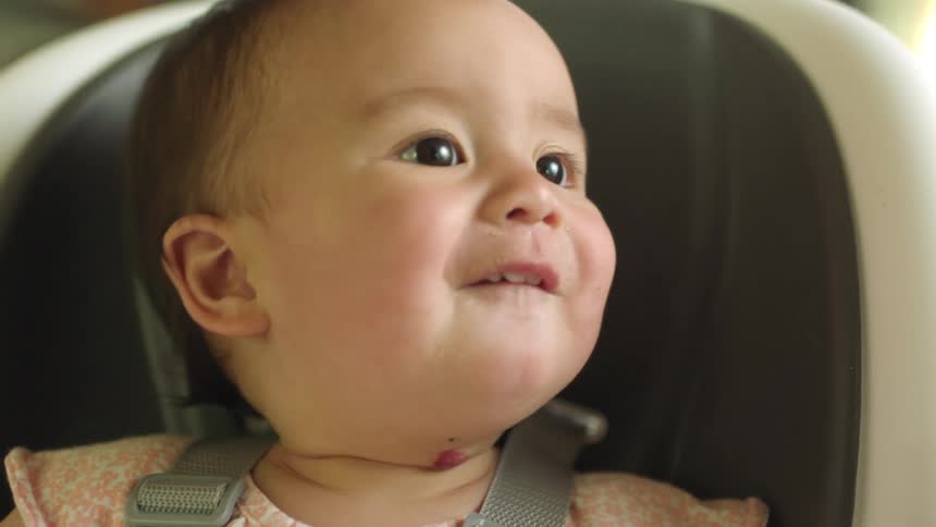 Mother feeds baby sitting in baby seat