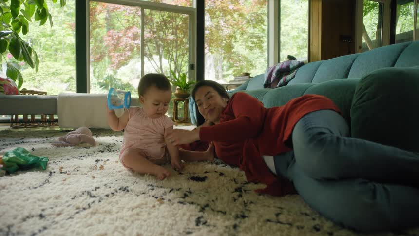 A woman and baby on the floor in a room with a couch and wall in the background
