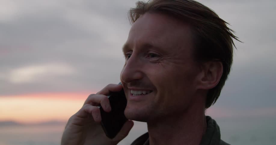 A man is outside talking on his cell phone and he looks around when he is done talking