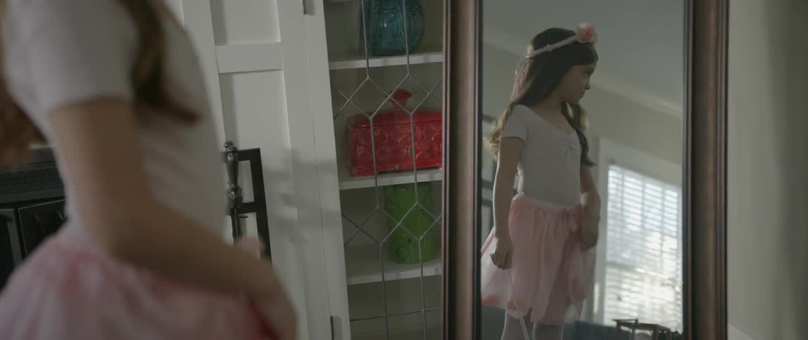 A girl in a ballerina costume stands in front of a mirror