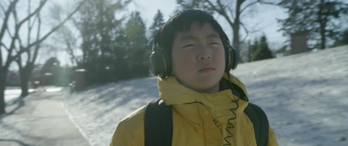 A boy in headphones walks down a snowy sidewalk