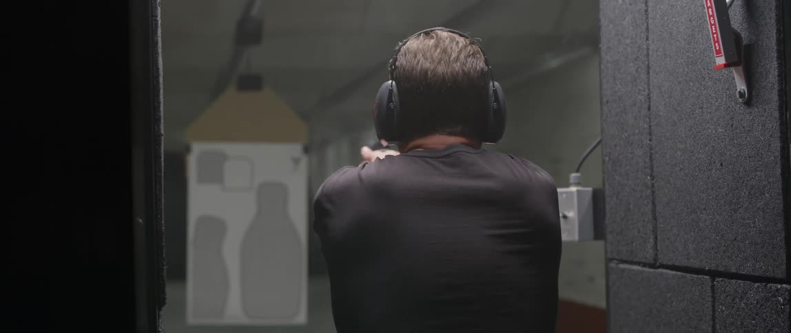 A man aims and fires a gun in a shooting range