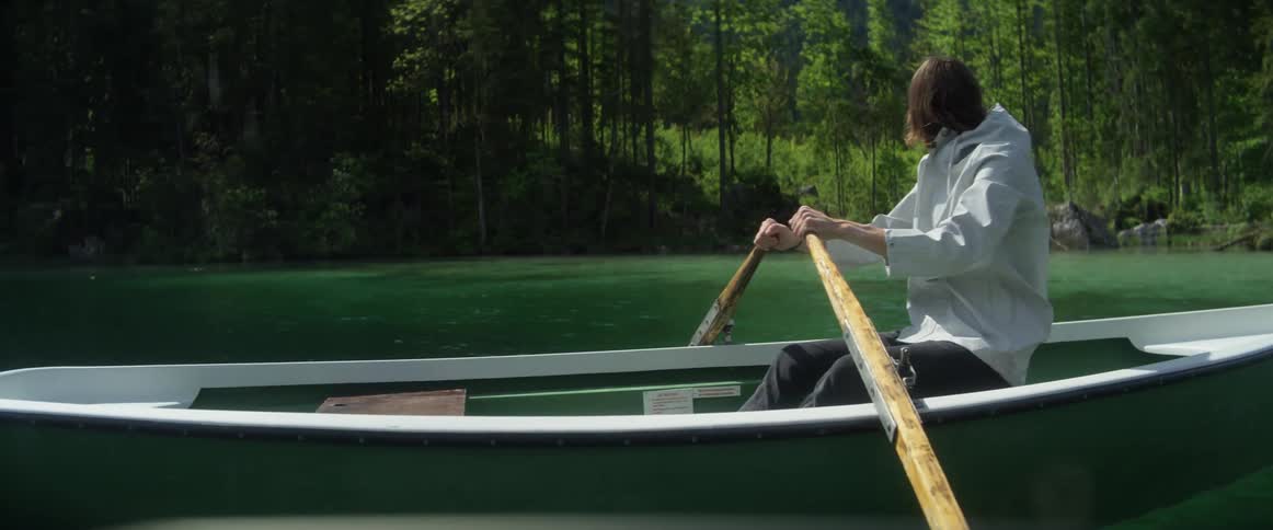 A young man is using oars and riding in a canoe on a lake