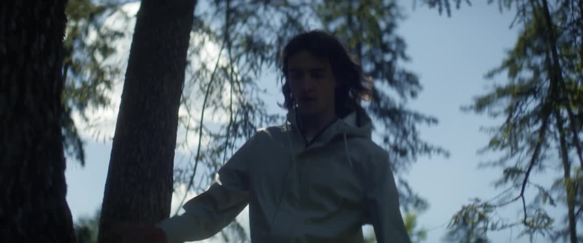 A young man is hiking through trees in the wilderness