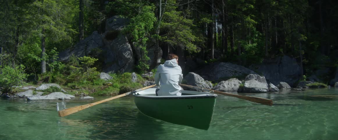 A man paddles a boat backward through clear river water