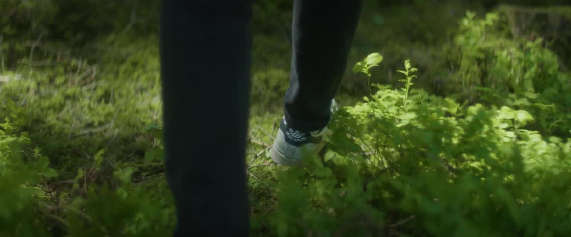The feet of a man walking through a woodland area in the daytime