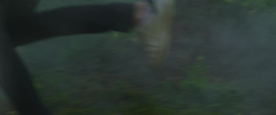 The legs and feet of a man running through a foggy woodland area in the daytime