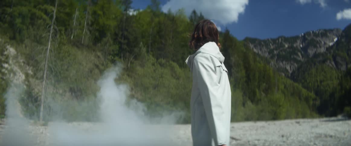 A man looks up and around at the mountains as smoke surrounds him