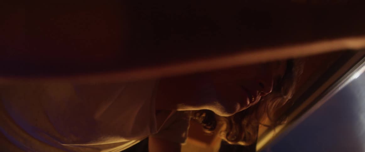 Man with long hair and white shirt looks up at street lights at night