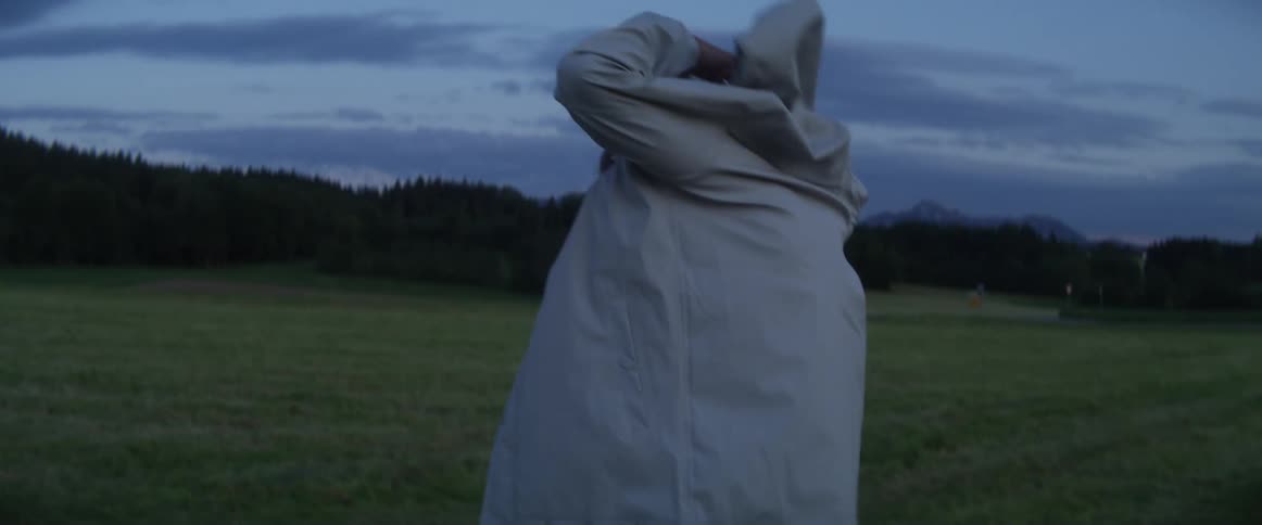 A teenage boy puts on a coat as he walks across a field