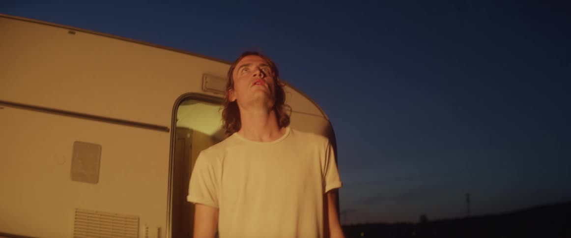 A man walking out of a camper and looking up at lights with the sky and clouds in the background