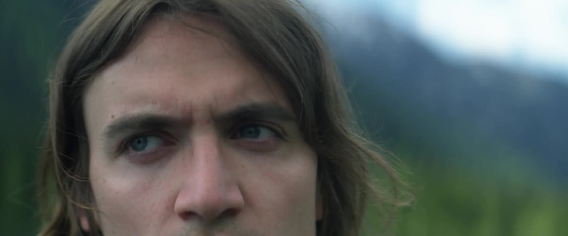 A man is standing near a wooded area and looks around
