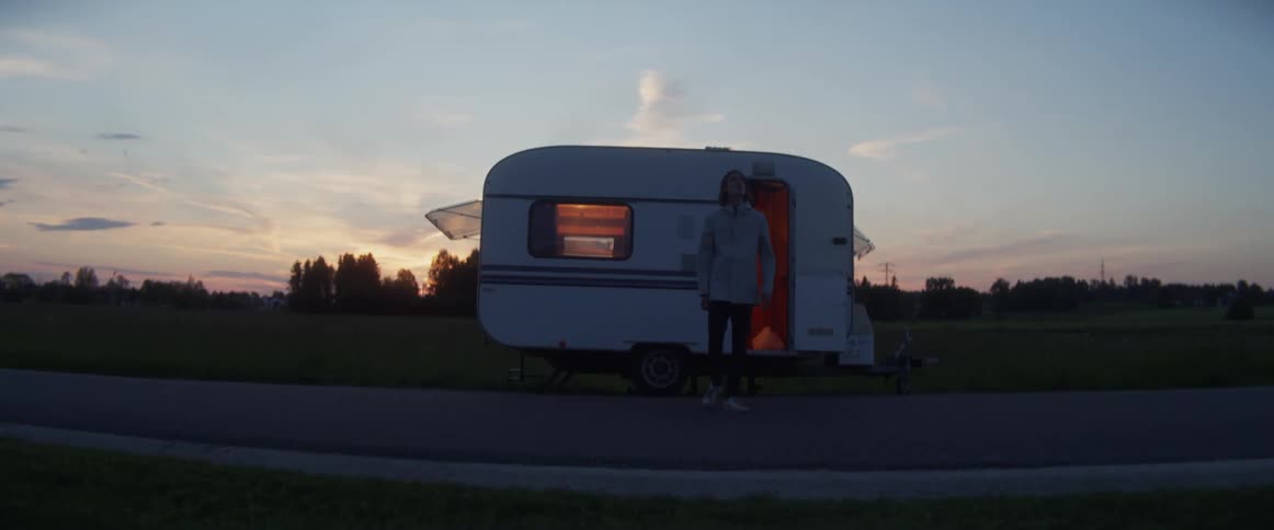 A man exits a roadside camper and walks away at dusk