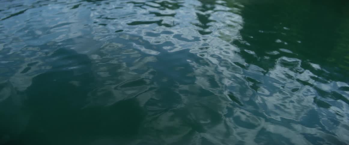The surface of a body of water is rippling with reflections of clouds