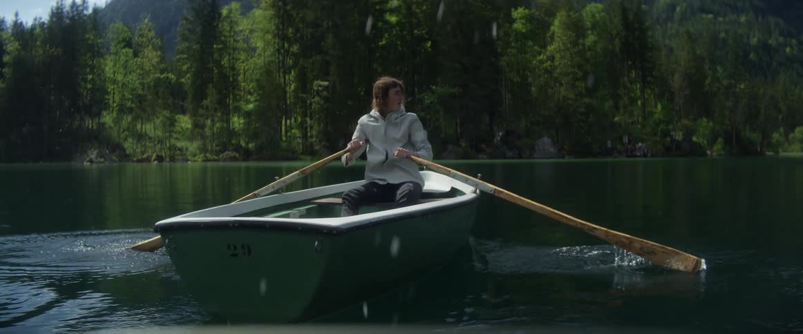A man paddles his boat backward in a lake