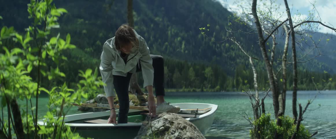A man stepping off of a boat with a mountain range the sky and clouds in the background