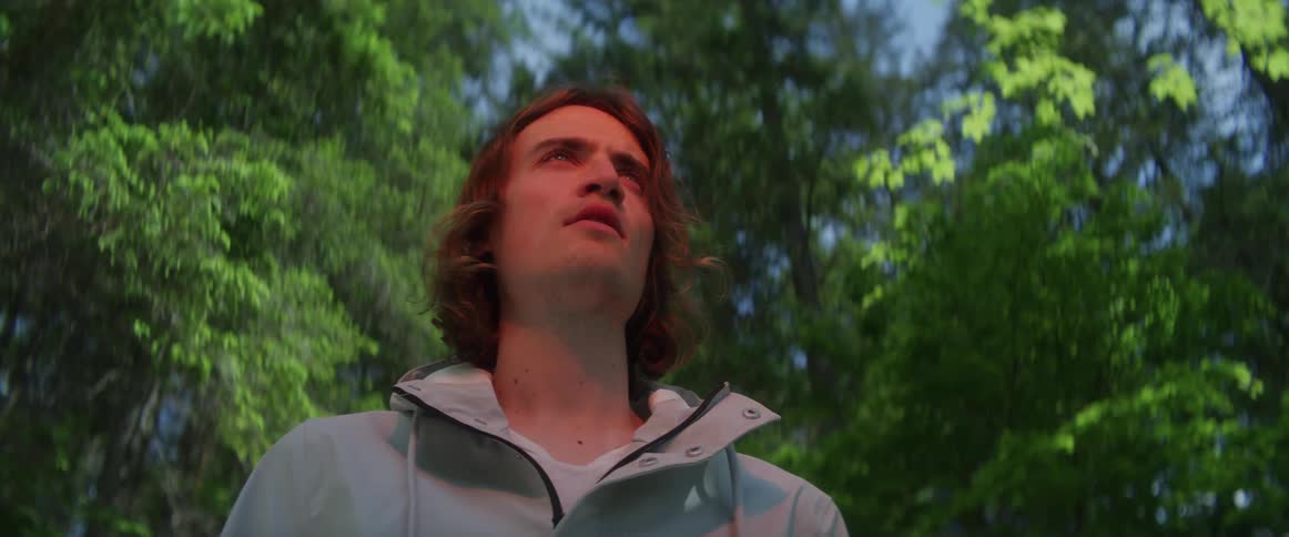 A young man standing and looking around alone in a green forest