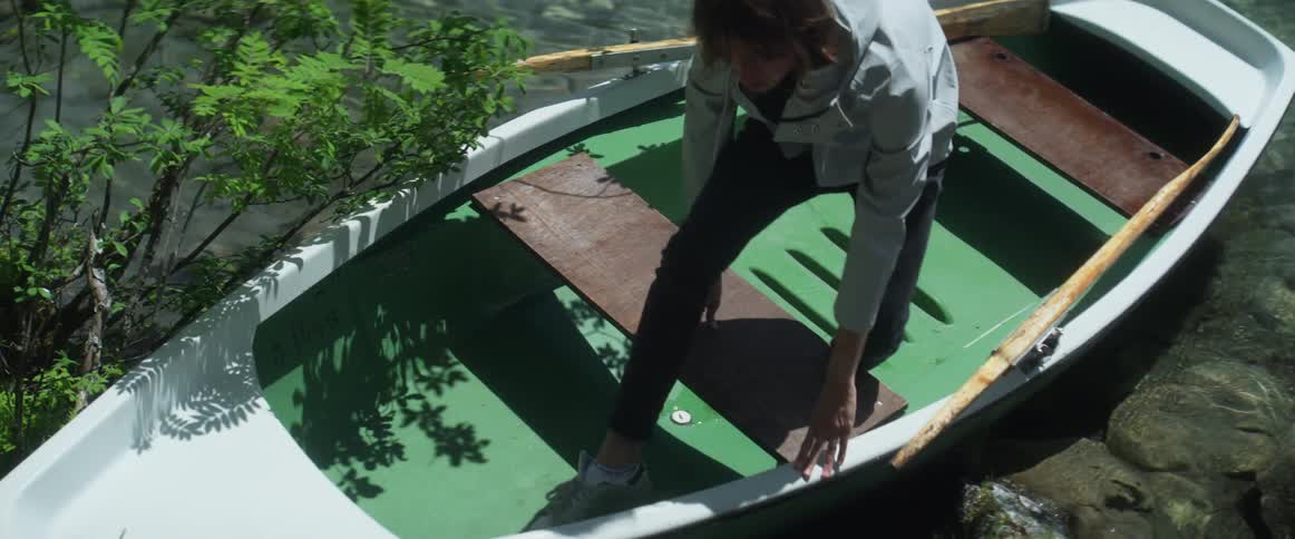 A person lands a rowboat on a rocky shore and exits from it
