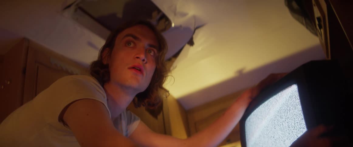 A man in a room hitting a television with a wall in the background
