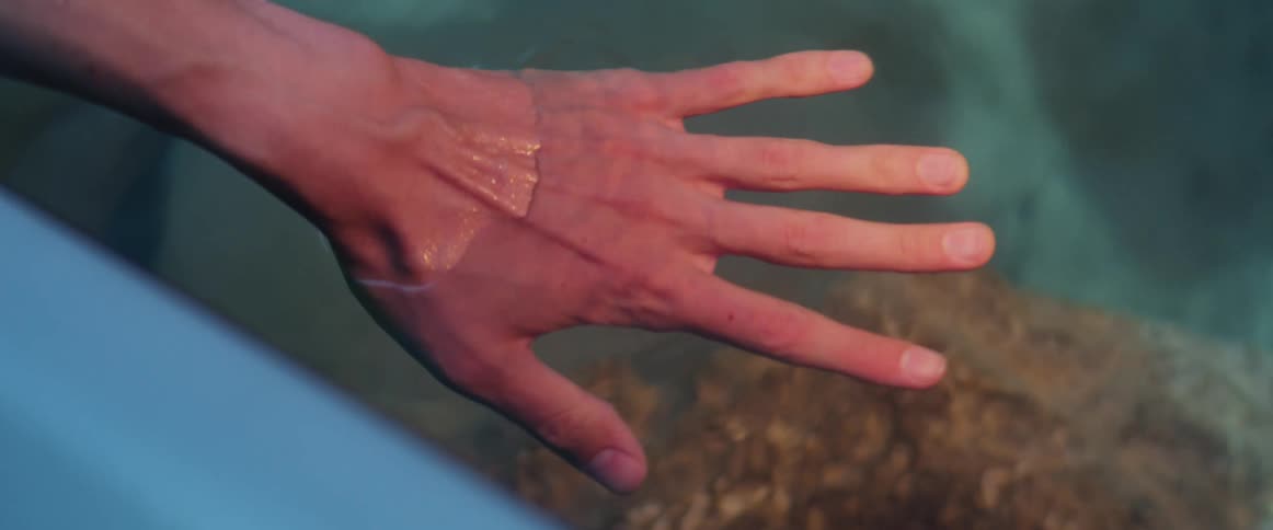 Person reaches hand into clear water showing rock while sitting near the water