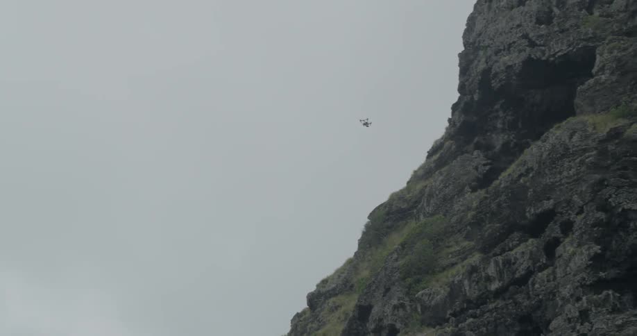 A drone flies up a cliff into a cave above
